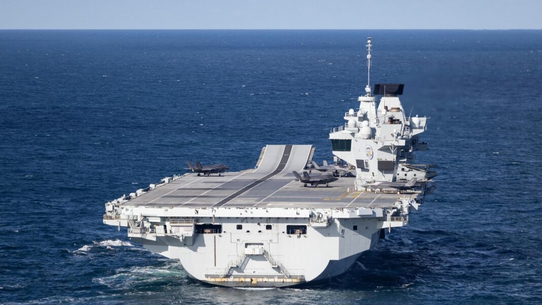 A large grey carrier is seen on the open ocean.