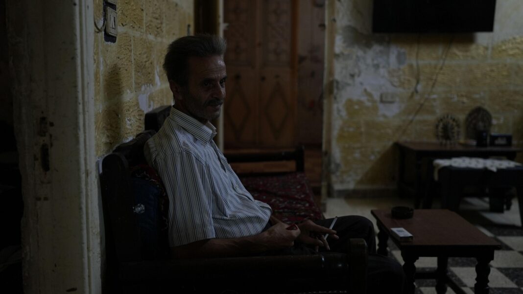 Syrians struggle with soaring prices as crisis challenges post-Assad recovery A man wearing a striped shirt sits in his living room in darkness