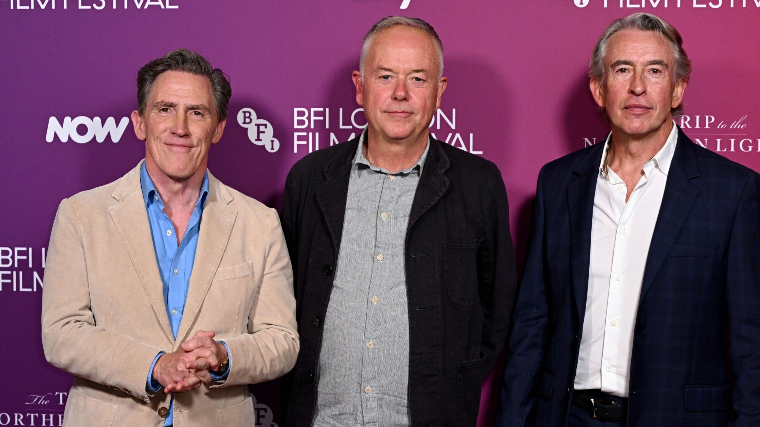 Rob Brydon (left), Michael Winterbottom (middle), and Steve Coogan (right) at a screening of The Trip to the Northern Lights. Brydon wears a beige suit jacket and a light blue shirt. Winterbottom wears a black jacket and grey shirt. Coogan wears a dark blue suit jacket with a white shirt.