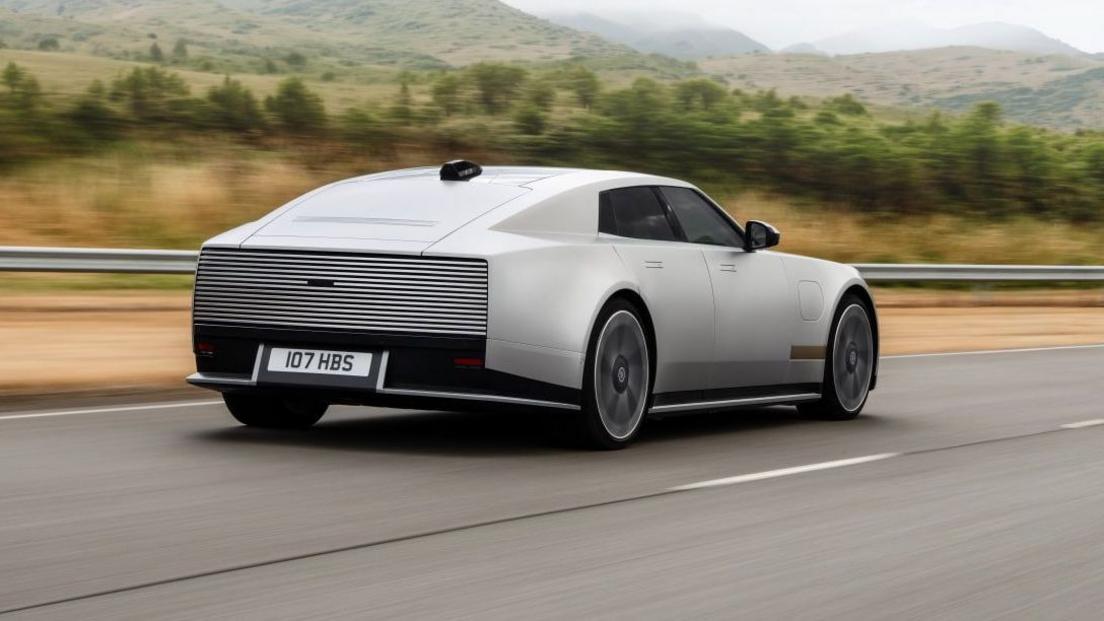 A silver version of the new Jaguar model driving along a road.