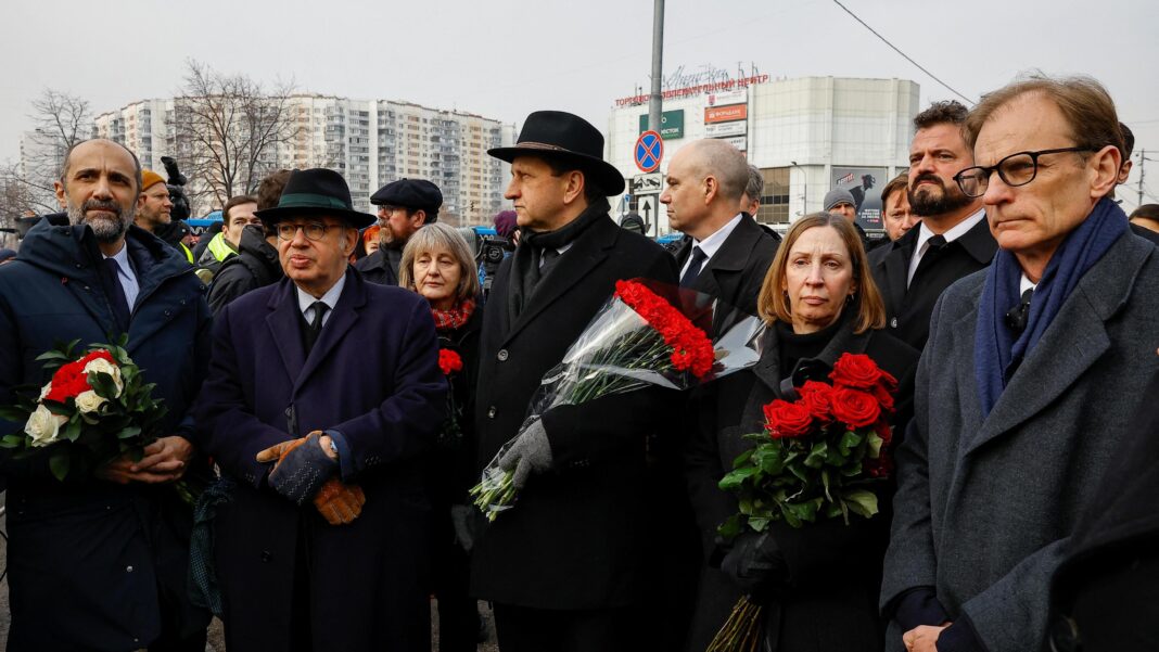 A number of people dressed in black coats and carrying red flowers are gathered together