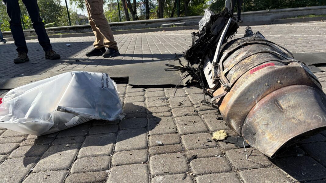 As freezing winter approaches, Kyiv residents look for shelter elsewhere Wrangled metal wreckage from a drone is seen on the pavement, with feet beyond.