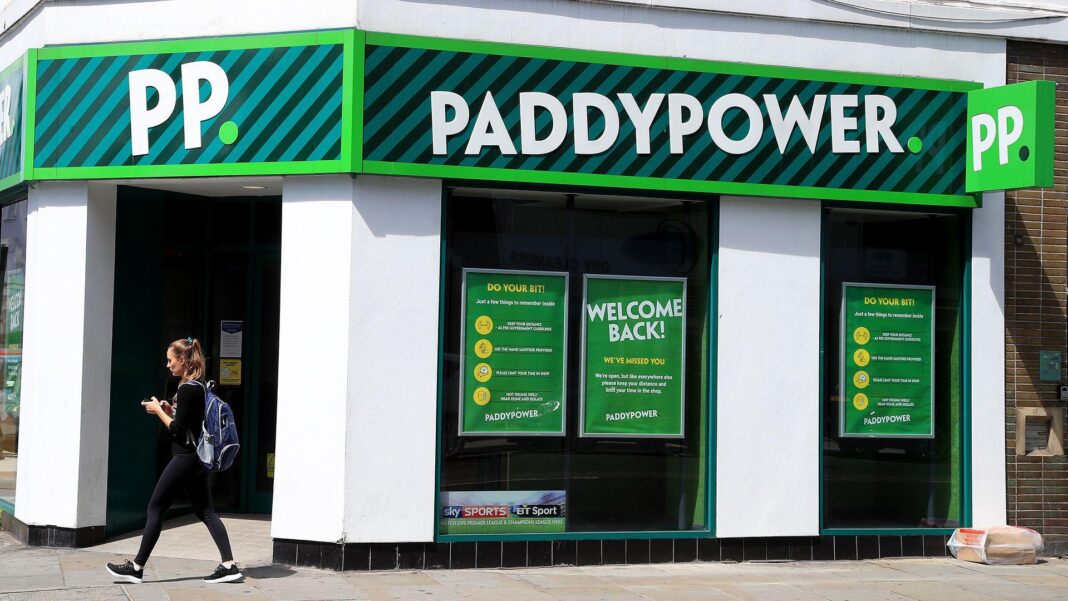 Paddy Power cuts 1,400 jobs and blames betting tax rises The Paddy Power logo is seen atop a storefront of a branch in London in 2020, with a person walking in front of it along the street looking at their phone on a sunny day.