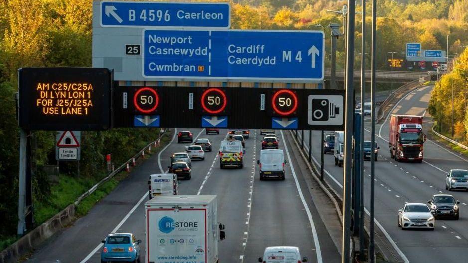 A scene from the M4 in Newport, with speed limits displayed on a screen and signs for Newport, Cardiff and Caerleon.