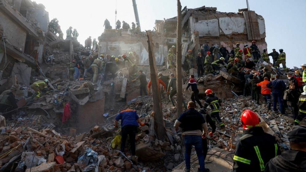 Emergency services work to rescue residents from under the debris at the site of an apartment building which was hit by a Russian missile strike in the town of Pryluky
