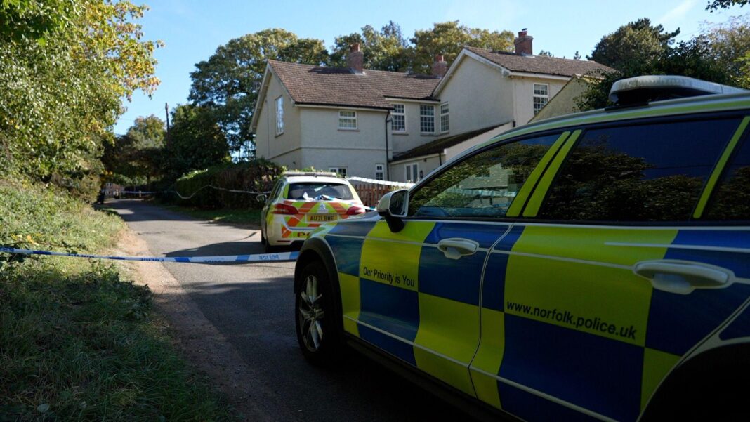 Two police cars outside a large property on a lane in a village.