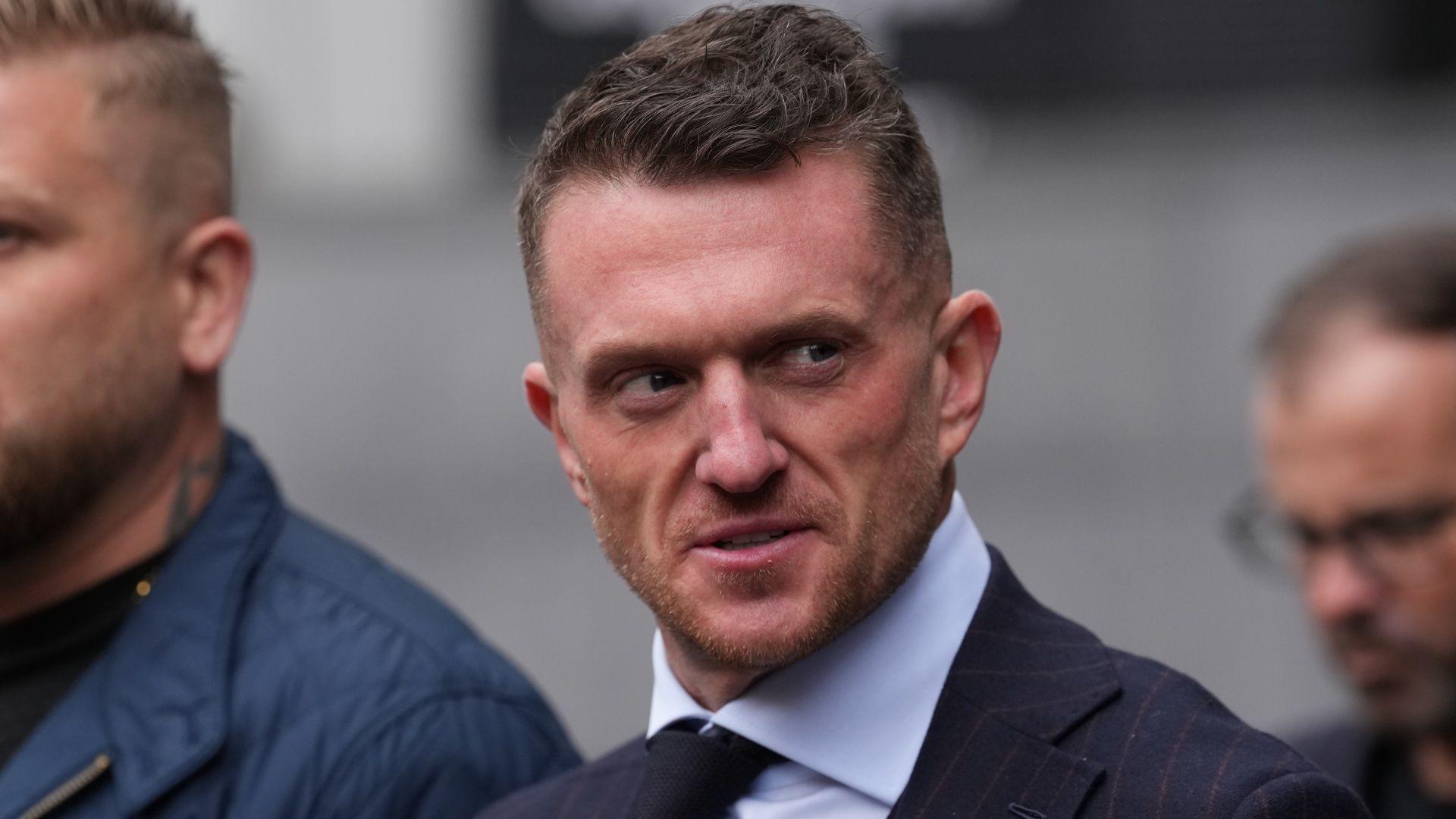 A close-up shot of Tommy Robinson outside court, wearing a white shirt, black tie and blue jacket.