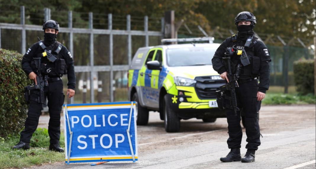 Armed police officers stand guard on a road outside the perimeter of the RAF Fairford airbase, after police declared a major incident at the base after several men were arrested near RAF Fairford