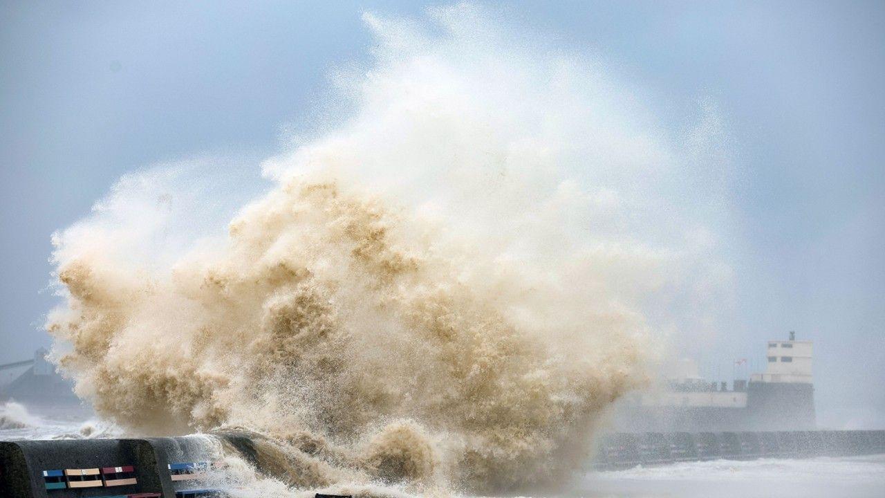 A wave crashes against the shoreline with grey sky overhead