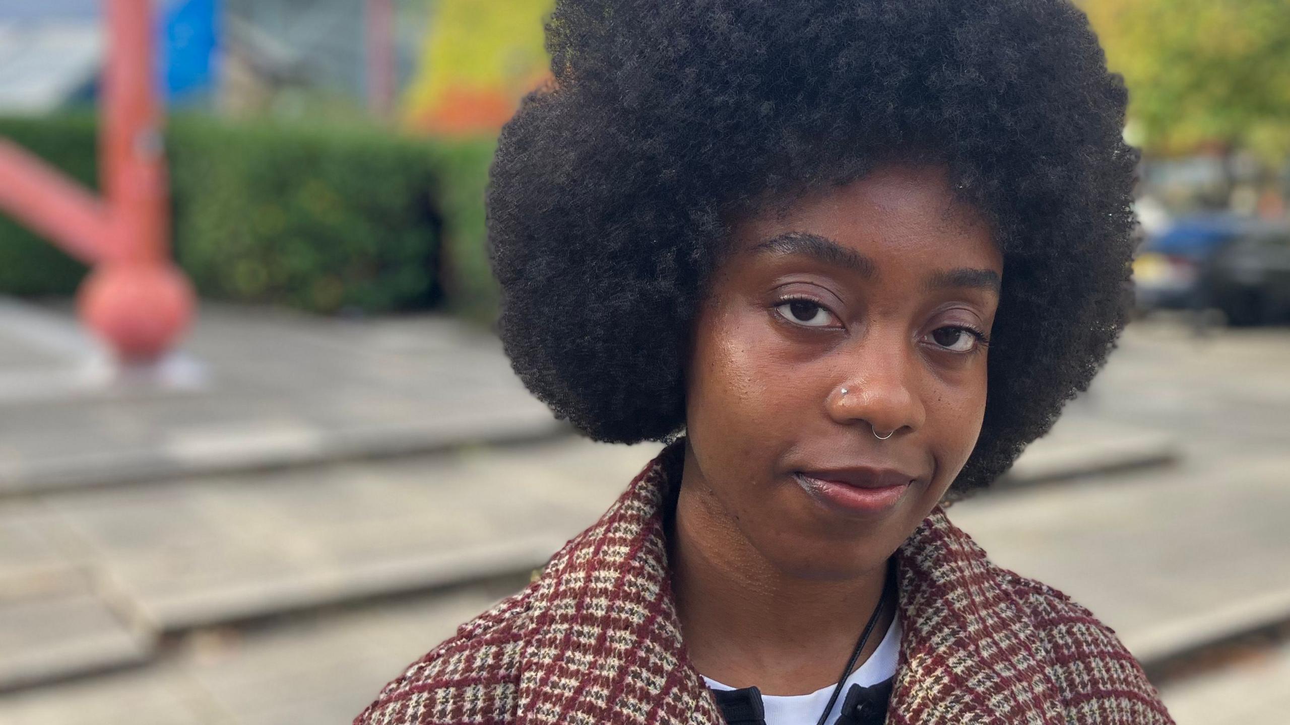 Poet Maureen Onwunali in a public plaza in Milton Keynes with trees and modern architecture in the background.