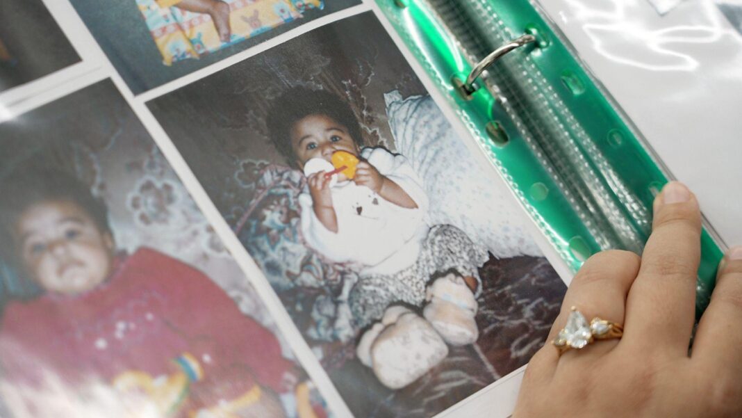 A hand opens the page of a photo album with pictures of a baby girl