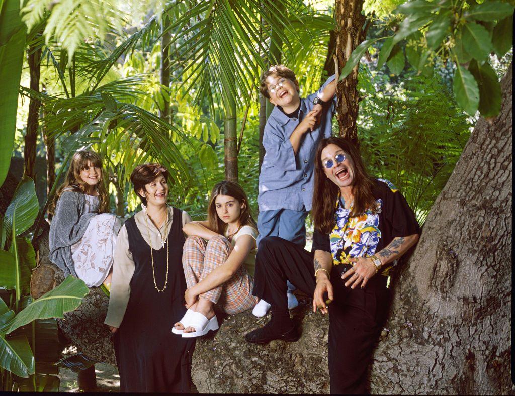 Osbourne family portrait when the children were young with members standing against and sitting on a tree in a forest