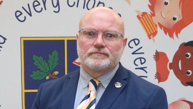 A man with a white beard, glasses and suit