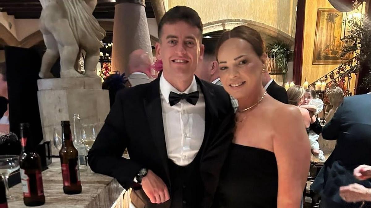 Josh Macdonald , wearing a suit and black tie, alongside his mum Clare, wearing a black dress, in a bar at what appears to be a black tie event like a wedding.
