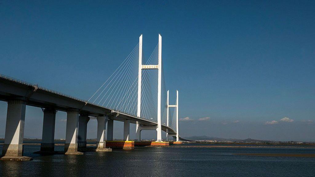 A cable-stayed bridge stretches across a broad body of water under a clear blue sky.