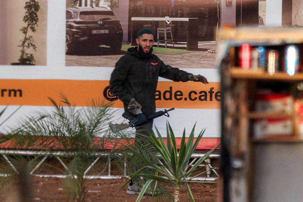 A gunman walks along in front of a billboard, holding an assault rifle.
