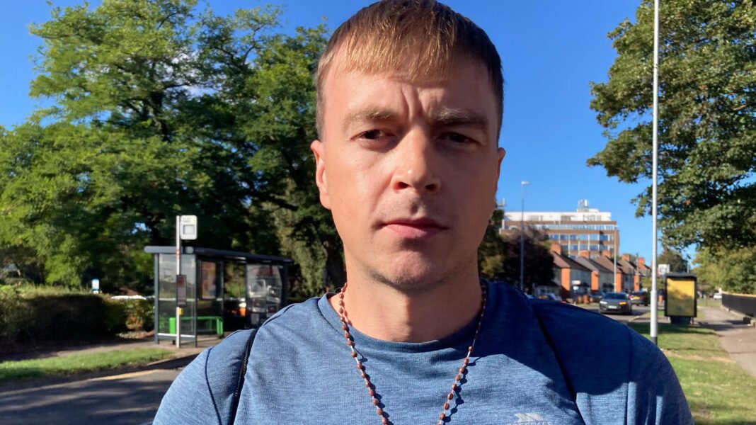 A man in his thirties wearing a t-shirt and crucifix necklace stood outside.