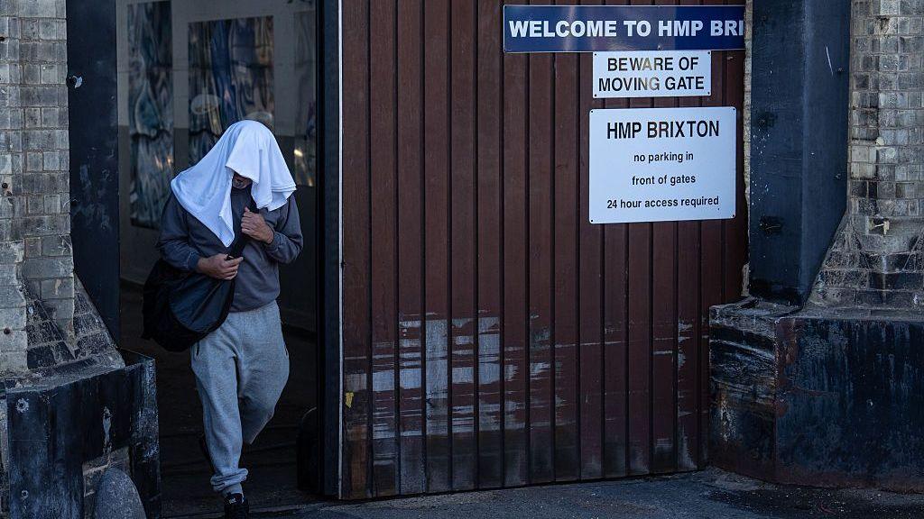 An inmate walks free from HMP Brixton with a while towel over his head