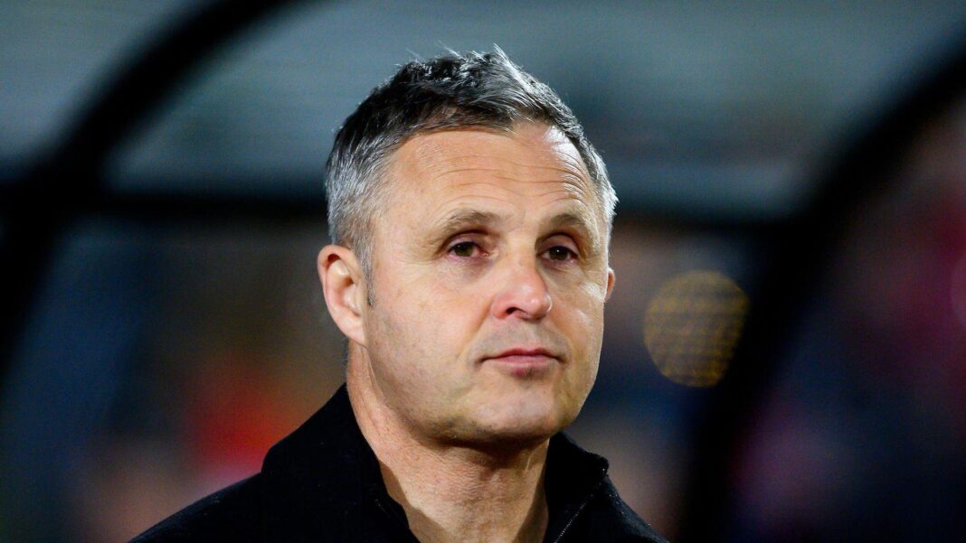 A headshot of Paul Rowley with a blurred view of a dugout in the background