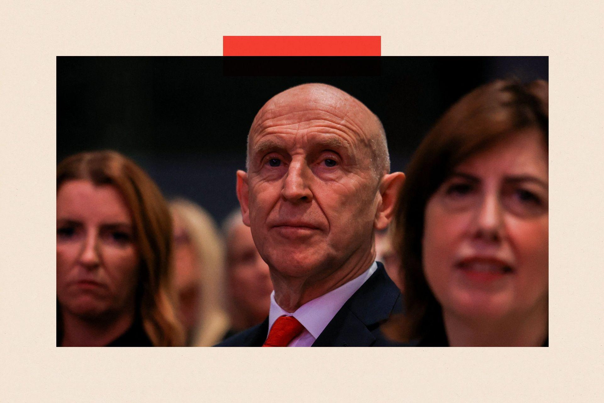 John Healey seated at the Labour Party conference. He is wearing a red tie.