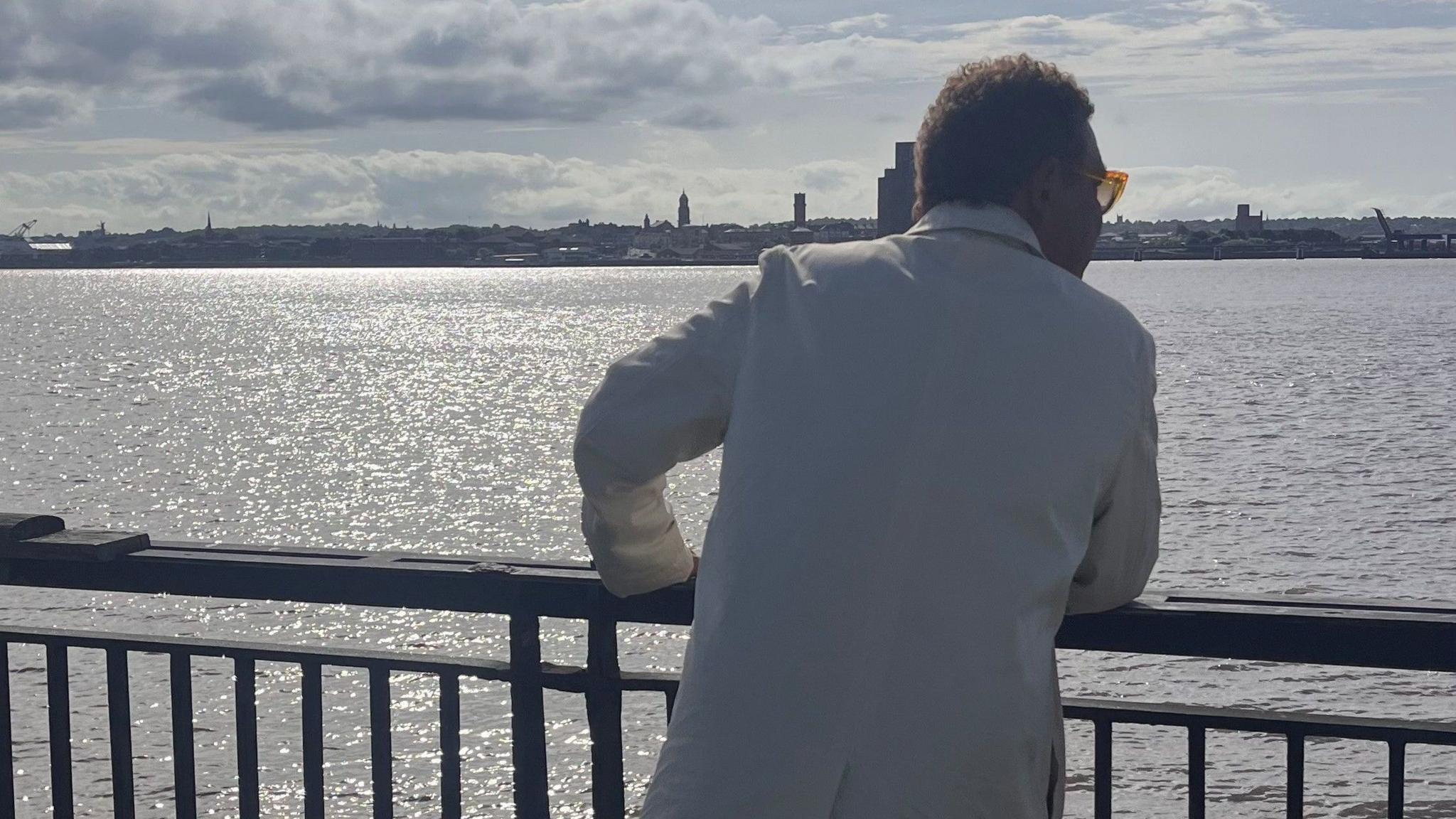 Craig, who is wearing sunglasses, leans on a railing as he looks out across the River Mersey.