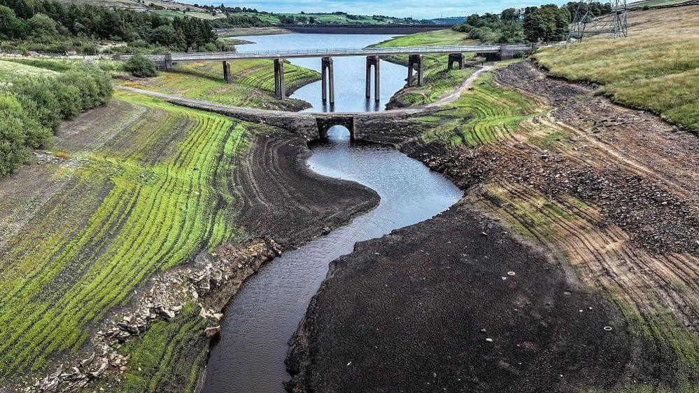 Aerial view of an ancient packhorse bridge revealed by low water levels and allows vegetation to grow on the bed of Baitings Reservoir near Ripponden, England