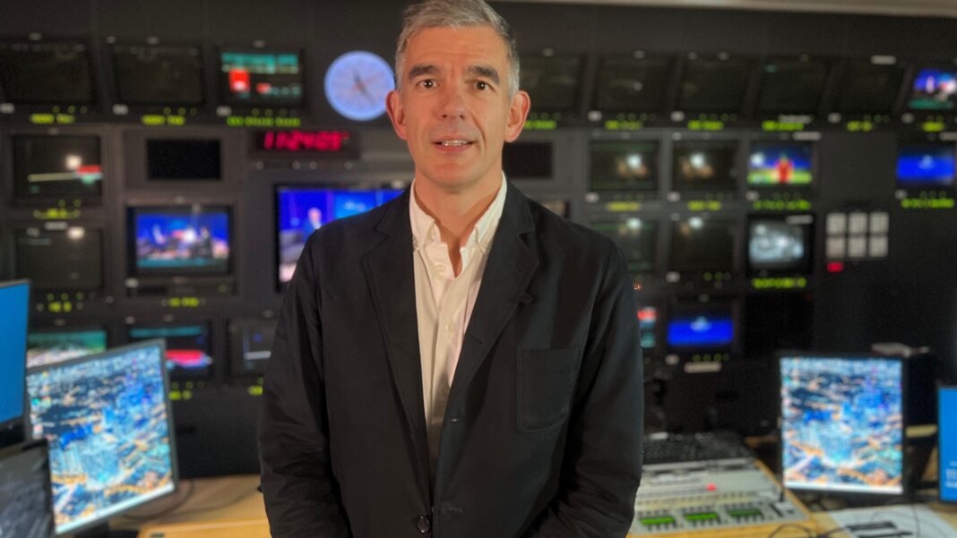 Dame Judi Dench joins Archers Birmingham campaign A man in a dark jacket and white shirt stands in a television control room, with rows of monitors, broadcast equipment and screens visible in the background.