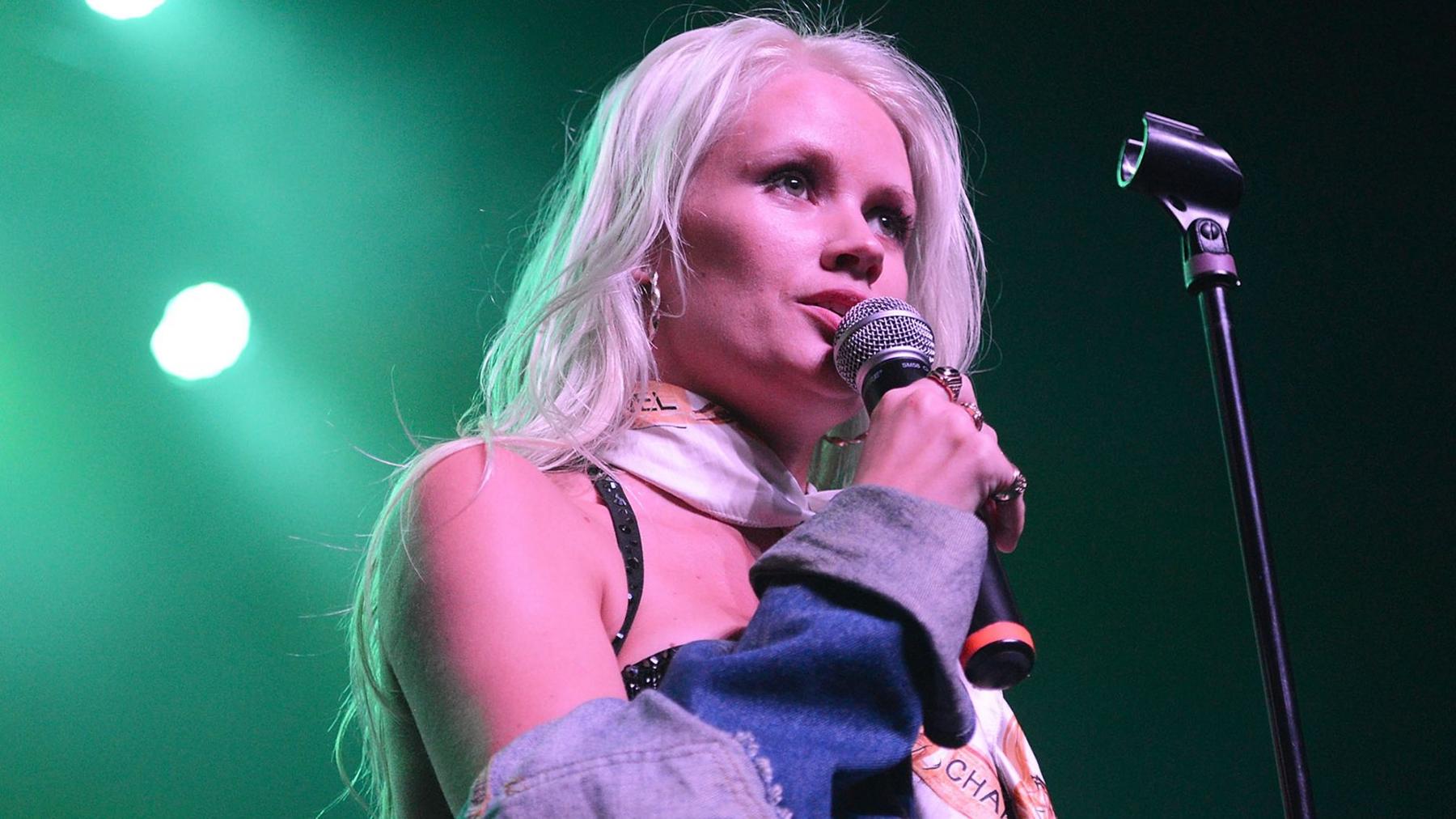 Lauren Bennett sings on stage during a concert. She has a demin jacket off her shoulsers and peroxide blonde hair