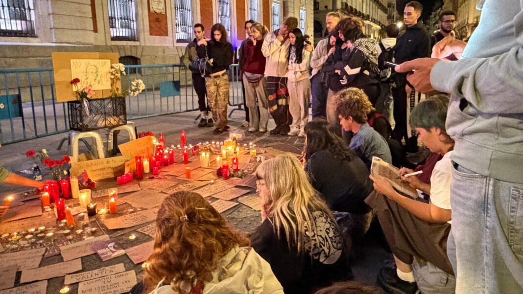 Spanish pensioner whose eviction sparked nationwide protests dies, union says People gather around a vigil where red candles and written tributes sit on pavement near a fence.