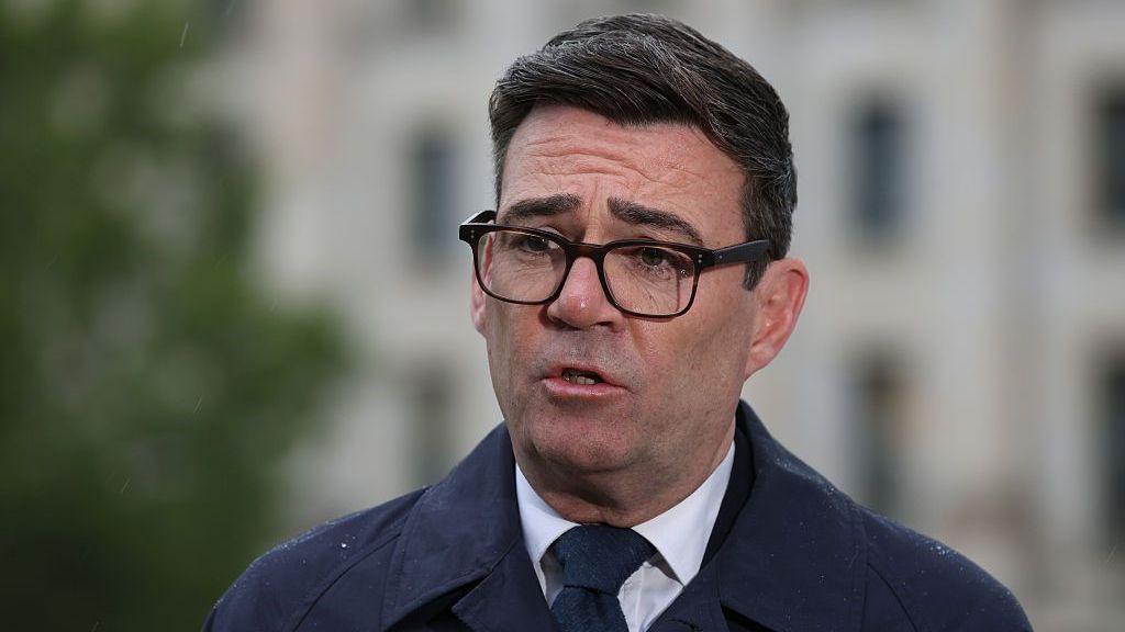 Andy Burnham, wearing a dark suit, recording a media interview in Berlin