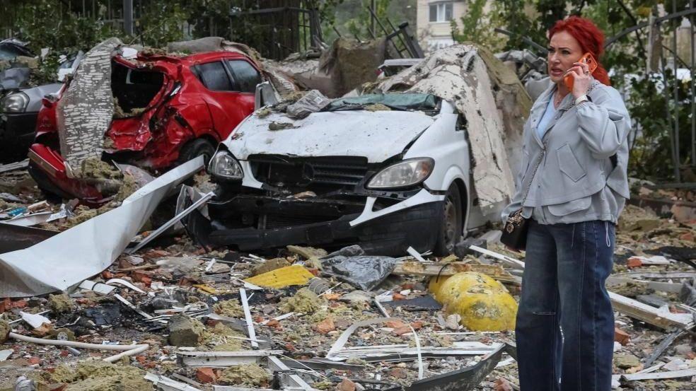 A woman in Ukraine's capital Kyiv talks on the phone near destroyed cars at the site of an apartment building damaged by a Russian strike. Photo: 26 October 2026