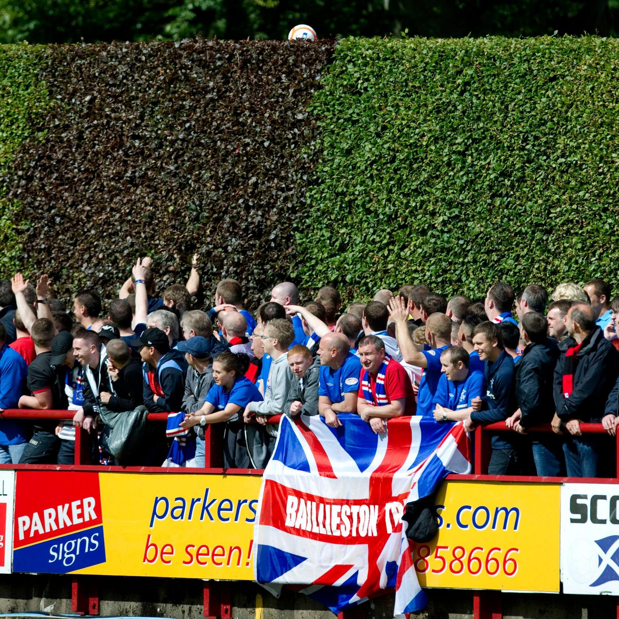 Rangers fans look at a ball sitting on top of a tall hedge at Glebe Park in Brechin