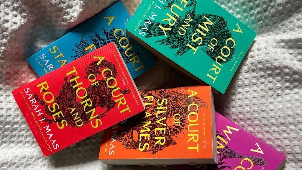 A photo of five different coloured booked on a bed.