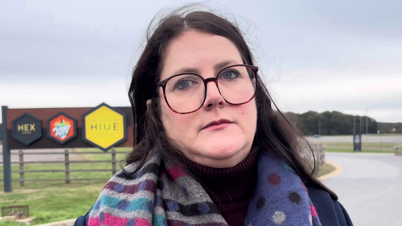 A woman with long black hair and large round glasses wearing a colourful scarf