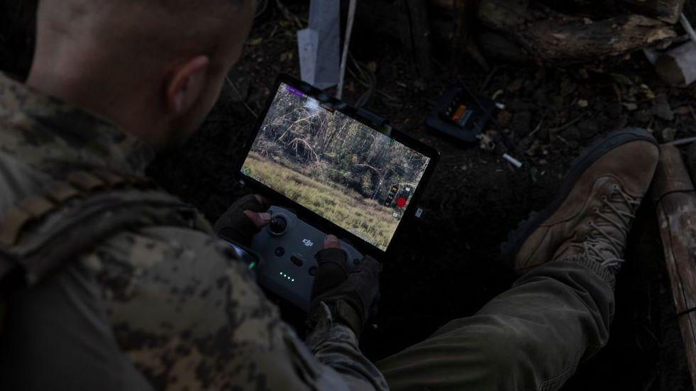 A solider rests a Starlink-connected phone on his body armour to communicate with other troops