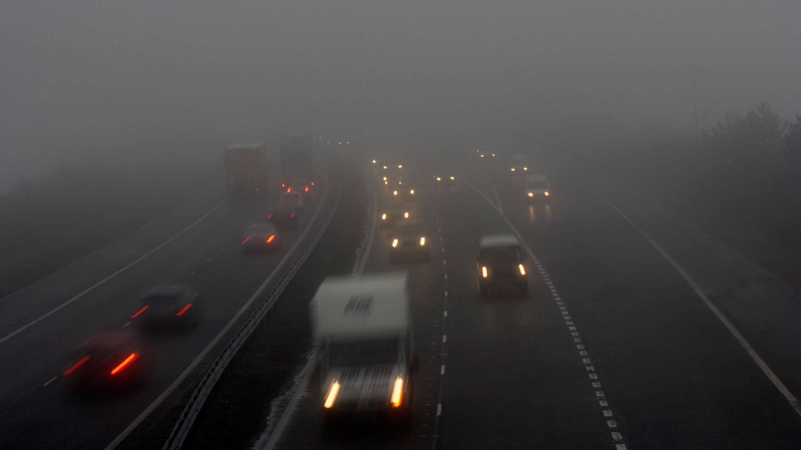 Photograph of vehicles including cars and vans on a dual carriageway road with their headlights on in foggy conditions.  Other cars are attempting to join the road from a slip road.