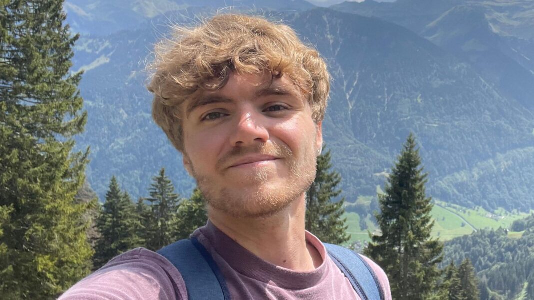 Is it OK for jobseekers or employers to use AI? A selfie style picture of Tom standing in a lush green landscape with mountains in the background. The 24-year-old wears a purple T-shirt and backpack.