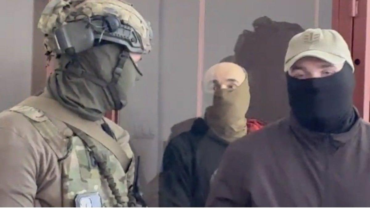 A blurred image of Vitalii Zhykovych in a cage - flanked by two masked men