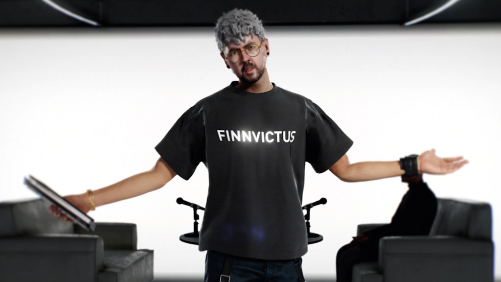 Screenshot from Hitman shows Jacksepticeye's character Finnvictus addressing a camera. He's standing in front of a bright white studio background, wearing a black t-shirt with his name printed on it in bold white capital letters. He's holding his arms out at his sides, gesticulating as he makes an impassioned speech.