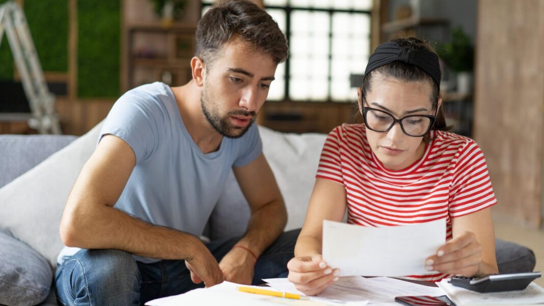 Tax thresholds remain unchanged – here’s what it means for your pay A young man and woman sit together on the sofa looking at paperwork