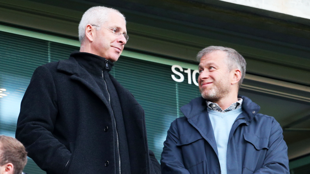Eugene Tenenbaum (left) stands alongside Roman Abramovich watching a match at Chelsea Football Club, in 2014. They are both wearing overcoats and smiling.