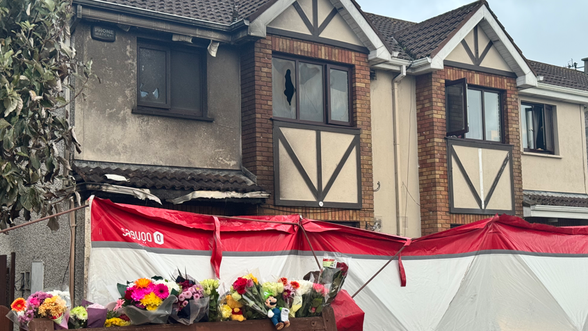 A house after a fire. Flowers and toys have been left outside.