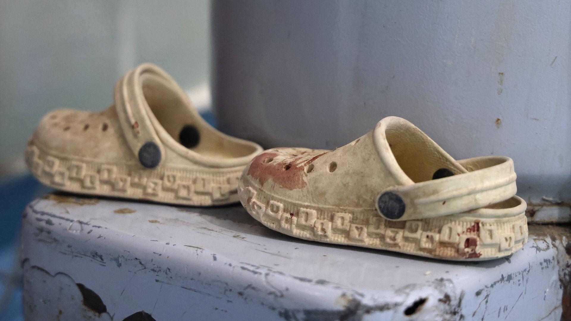 A pair of child's beige, rubber sandals, with splatters of blood.