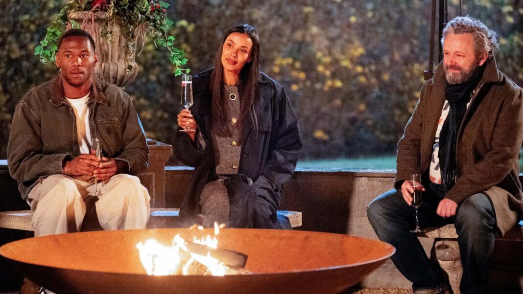 King Kenny, Mya and Michael Sheen sit tentatively around the firepit on the penultimate night of The Traitors