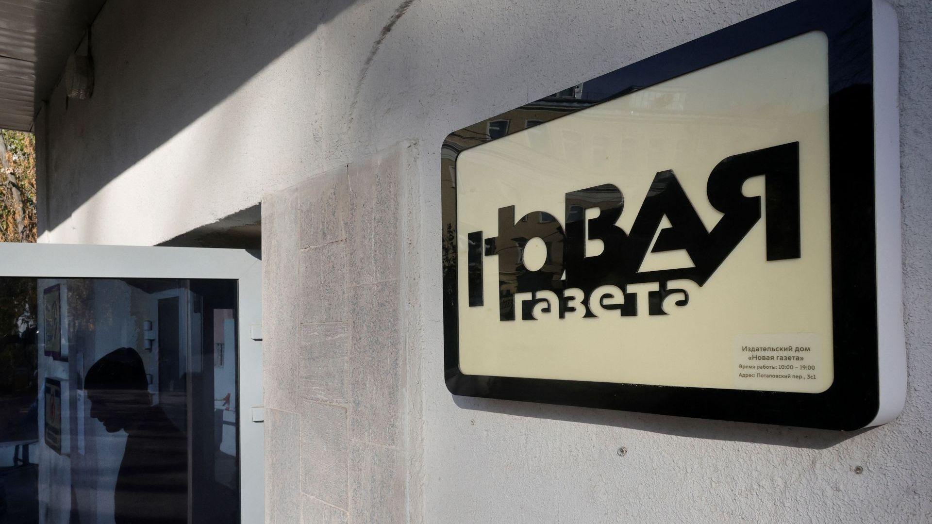 A grey building with Novaya Gazeta's logo in Russian. The door is open with a silhouette of a person walking out on October 30, 2026