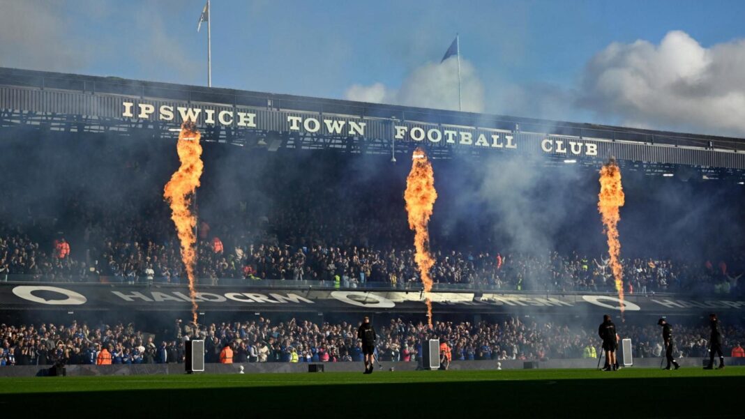 Ipswich supporter ‘feared for life’ when Maidstone fan fell on her from stand above A two-tiered stand at a football ground. It has "IPSWICH TOWN FOOTBALL CLUB" in white letters on the front of the roof. Between the upper and lower tiers is a sloping roof over executive boxes which has advertising on it. There are three flames rising from devices on the pitch that reach the roof of the stand. The stand is full of supporters.