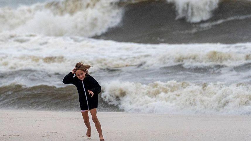 A girl running on Orange beach in Alabama. Her hair is blowing in the wind and the water behind her is turbulent