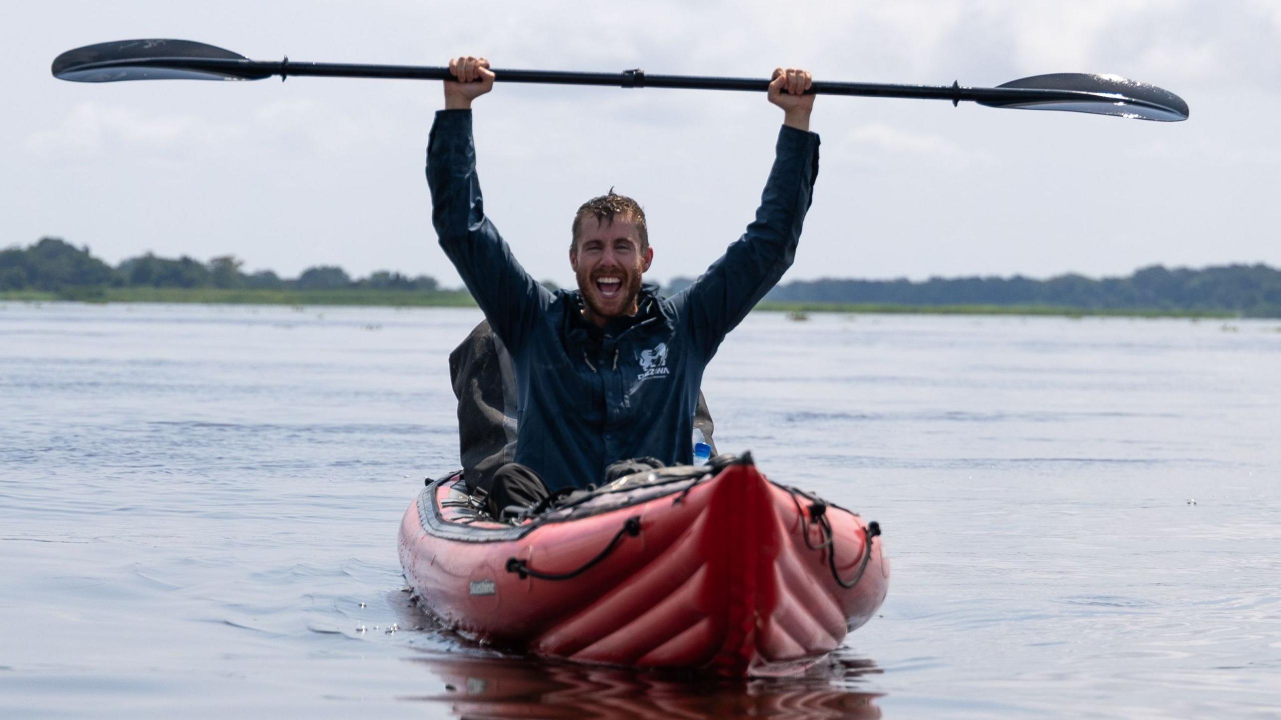 Ash Dykes in his kayak raising his paddle in triumph after completing his 700 kilometre trek through the Congo Basin