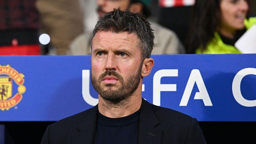 Michael Carrick, wearing a black T-shirt and black blazer, looks on from the dugout during a Champions League match