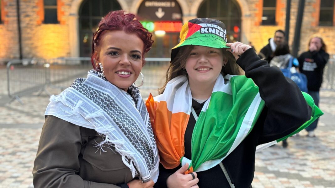 Macklemore begins Free Palestine tour after Ed Sheeran fallout Nicola McCollough, who has red hair tied back and wears silver-coloured hoop earrings, a keffiyeh scarf and a brown jacket. Her daughter Lily Rose stands to her left wearing a black hoodie, a bucket hat in the colours of the Palestine flag and with the Kneecap logo on it and an Irish tricolour around her shoulders.